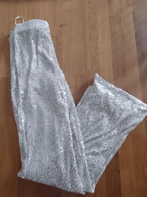Silver/beigea paljettleggings med glitter - Glittriga leggings i silver/beige med täckande paljetter över hela tyget. De har en elastisk midja och raka ben, vilket ger en snygg och bekväm passform. Perfekta för dig som vill sticka ut och glänsa lite extra. Materialet är stretchigt och följsamt.