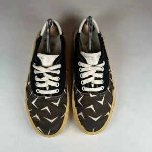 Saint Laurent svarta låga sneakers - Snygga låga sneakers från Saint Laurent med svart canvas, vita grafiska mönster och vita snören. Skorna har beige gummisula och vita detaljer vid hälen. 39,5 men stora i stl så passar 40.5 Perfekta för dig som vill ha en stilren men unik look. Små tecken på användning. Nypris 6500 kr!