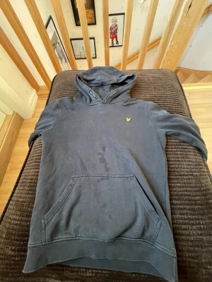 Mörkblå hoodie från Lyle & Scott - Snygg mörkblå hoodie från Lyle & Scott med klassisk gul logga på bröstet. Hoodien har känguruficka framtill och en mjuk, bekväm känsla. Perfekt för en avslappnad stil och enkel att matcha med jeans eller joggers.
