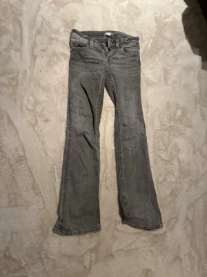 Lågmidjade bootcut Gina Tricot  - Gråa lågmidjade bootcut jeans från Gina tricot. En knapp är borta men annars bra skick, säljer bara för att de inte passar längre. Storlek 164, typ xs-xxs