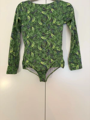 Body topp - Snygg långärmad body  med tropiskt blad- och bananmönster i olika gröna nyanser. Djup rygg och rundad halsringning framtill. 