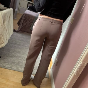 Bruna kostymbyxor med raka ben - Säljer ett par stilrena bruna kostymbyxor med raka ben Byxorna har pressveck, hällor för skärp och stängs med knapp och dragkedja. Perfekta för en clean och trendig look.