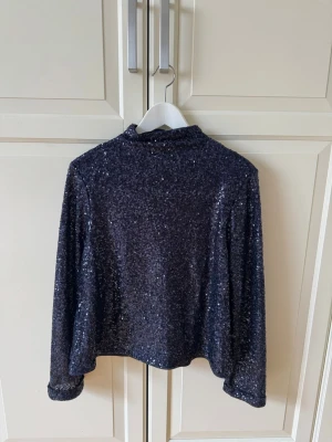 Svart glittrig polotopp - Snygg svart polotopp täckt med glittriga paljetter. Toppen har lång ärm och en hög krage 