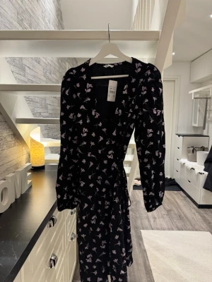 🌸 Jättefin omlottklänning med blommönster - Säljer en superfint mönstrad klänning i omlottmodell. Klänningen har långa ärmar med lite puff vid axeln och ett vackert fall. Perfekt till både vardag och festligare tillfällen! 🌸 • Varumärke: Cubus • Storlek: Small  • Modell: omlottklänning • Färg: Svart bas med ljuslila/rosa blommönster • Skick: Ny med prislapp kvar (se bild) Klänningen knyts i midjan vilket ger en väldigt smickrande passform. Materialet känns lätt och behagligt. Pris: 100 Hör av dig om du har några frågor! Jag skickar spårba