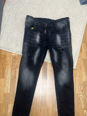 Svarta skinny jeans från Dsquared2 - Säljer ett par svarta jeans från Dsquared2 med slitningar och tvättade detaljer på låren. Jeansen har klassisk femficksmodell och Dsquared2-logga bak vid linningen. Materialet är stretchigt för en bekväm passform.
