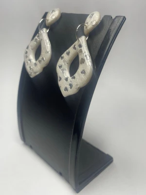 Silvriga örhängen med hjärtmönster - Unika örhängen i silvrig färg med droppformad design och små hjärtan i metallic. Tillverkade i ett lätt material som liknar lera eller resin. Perfekta för dig som vill sticka ut med ett coolt och trendigt smycke.