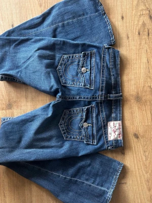 Blå True Religion jeans bootcut - Säljer ett par blå jeans från True Religion med klassiska kontrastsömmar och vida ben. Sparsamt använda så i väldigt fint skick 💕 storlek 27 i modellen Joey