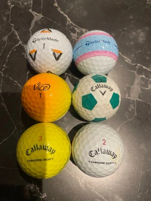 6 olika golfbollar från Callaway, TaylorMade, Vice - Säljer ett set med 6 golfbollar från Callaway, TaylorMade och Vice. Bollarna är i olika färger: vit, gul och orange, samt har olika mönster och tryck. Några har färgade linjer och en har fotbollsmönster. Perfekt för dig som vill ha variation på golfbanan.