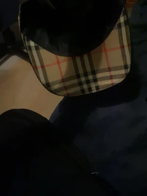 Burberry klassisk rutig keps - Säljer en ikonisk keps från Burberry med det klassiska beigea rutmönstret med svarta, vita och röda linjer. Kepsen är tillverkad i bomull och har en böjd skärm. Märket Burberry syns tydligt på insidan. Perfekt accessoar för en trendig streetwear-look.