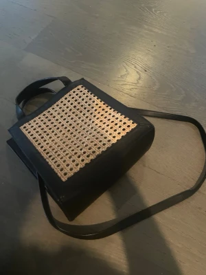 Cool vintage väska❤️ - Snygg ryggsäck med svart konstläder och framsida i flätad rotting. Rektangulär form med långa axelband och ett praktiskt handtag upptill. Perfekt för dig som gillar en unik och trendig look. Handtagen lite slitna men syns eller stör knappt❤️