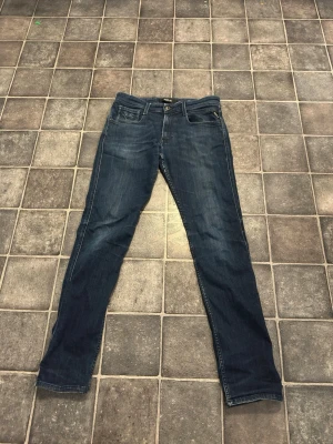 Mörkblå jeans från Replay - Snygga mörkblå jeans från Replay med klassisk femficksmodell och raka ben. Jeansen har diskreta slitningar och Replay-logga på bakfickan. Tillverkade i mjuk denim som ger en bekväm passform och cool look.