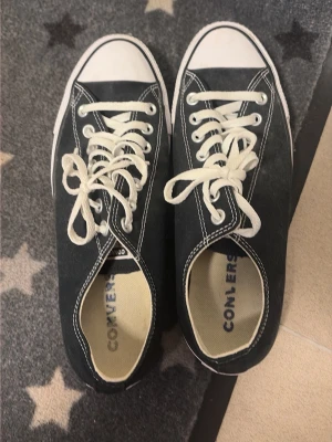 Svarta Converse låga sneakers - Klassiska svarta Converse sneakers med vit tå och vita snören. Skorna har kontrastsömmar och den ikoniska Converse-loggan på innersulan. Ovandelen är i canvas och sulan är i gummi. Perfekta för en avslappnad och cool stil. Används nån gång här och där men i väldigt bra skick