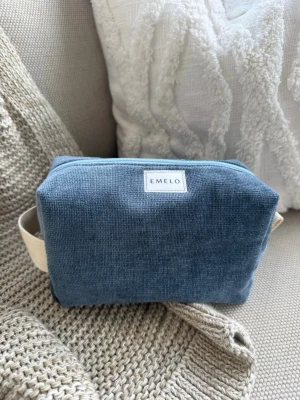 Blå necessär från Emelo i tyg - Säljer en stilren blå necessär från Emelo i mjukt möbeltyg. Väskan har en rektangulär form, ljusblå dragkedja och praktiskt handtag i beige tyg på sidan. Perfekt för att organisera småsaker eller smink i väskan. Storlek medium. Mått ca 20x12x8cm 