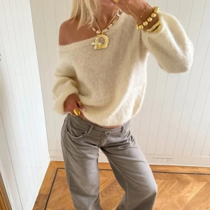 Off shoulder krämvit stickad tröja - Trendig off shoulder stickad tröja i krämvitt med avslappnad passform och långa ärmar. Mjuk och fluffig kvalitet, perfekt att styla med smycken och jeans. Bilder från hemsidan