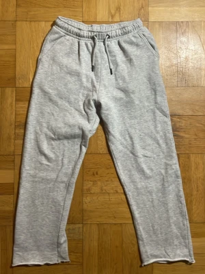 Ljusgrå mjukisbyxor med dragsko - Ljusgrå mjukisbyxor med resår i midjan och justerbar dragsko. Byxorna har raka ben och två sidofickor. Tillverkade i mjukt sweatshirtmaterial som känns skönt mot huden. Perfekta för chill dagar eller när du vill vara bekväm.