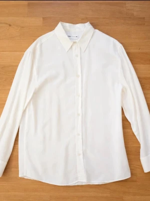Vit klassisk skjorta från Zara - Stilren vit skjorta från Zara med klassisk krage och knäppning framtill. Skjortan har lång ärm och är tillverkad i ett mjukt material som känns skönt mot huden. Perfekt basplagg för garderoben och lätt att matcha till olika looks.