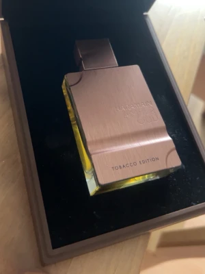 Al Haramain Amber Oud Tobacco Edition - Amber Oud Tobacco Edition från Al Haramain är en exklusiv parfym i en elegant, fyrkantig glasflaska med metallock i kopparfärg. Doften har en djup gul vätska och flaskan har en lyxig, modern design med ingraverad text på framsidan. Säljes för att jag har på tok för många vinterdofter.
