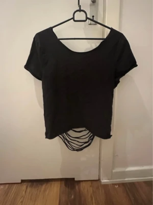 Svart croppad topp med öppen rygg med snören - Svart lite cropped tröja med öppen rygg med snören. Halsringen e oval så oftast är den på bara en axel! Använt några gånger men inte min stil längre. (Säljer även på vinted)