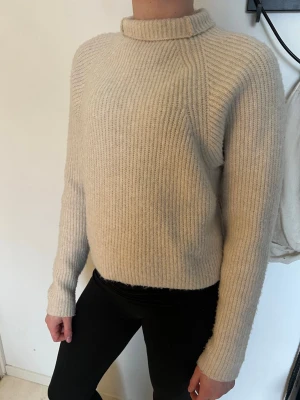 Beige ribbstickad tröja  - Säljer en beige ribbstickad tröja med hög krage och långa ärmar. Tröjan har en rak passform och är gjord i ett mjukt, tjockt material som känns riktigt mysigt. Perfekt för kyliga dagar och enkel att matcha med allt.