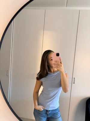 Ljusblå tight t-shirt - Säljer en ljusblå t-shirt med tight passform och korta ärmar. T-shirten har en enkel, stilren design utan synliga loggor eller mönster och är tillverkad i ett mjukt bomullsliknande material. Perfekt till jeans eller kjol för en clean look.