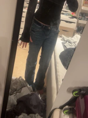 Blå bootcut jeans med slitning - Ett par blå bootcut jeans med lätt slitning och klassisk femficksmodell. Jeansen har en något utsvängd passform nedtill och normal midja. Perfekta för en avslappnad och trendig look.