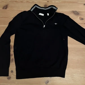 Svart half zip tröja från GANT - Svart långärmad tröja från GANT med half zip och ribbad krage med gråa ränder. Broderad GANT-logga på. Helt ny utan prislapp aldrig andvänd, nypris är drygt 700. Hör av er vid frågor mvh Victor 