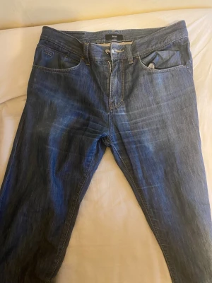Mörkblå jeans från HUGO BOSS - Snygga mörkblå jeans från HUGO BOSS med klassisk femficksmodell och raka ben. Jeansen har subtila slitningar och kontrastsömmar som ger en cool look. Tillverkade i mjukt denimtyg som sitter skönt hela dagen. 