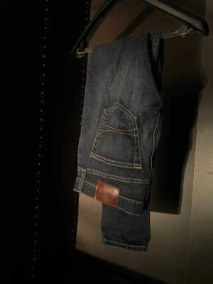 Mörkblå slim fit jeans från Hollister  - Snygga mörkblå jeans i slim fit-modell från Hollister , med kontrastsömmar och klassiska fem fickor . Jeansen har en läderpatch bak i midjan och subtila slitningar framtill för en trendig look. Perfekta för dig som gillar en stilren men avslappnad vibe.