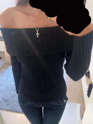 Svart ribbad offshoulder stickad topp - Säljer en svart stickad topp med ribbad struktur och offshoulder-design. Tröjan har lång ärm och sitter tight. Perfekt att styla med jeans eller kjol för en trendig look.