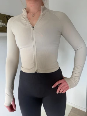Beige ziptröja från amin - Snygg beige ziptröja från amin med lång ärm och tumhål. Tröjan är croppad och har en smal passform, perfekt för träning eller chill. Tillverkad i stretchigt funktionsmaterial som andas🔥🔥