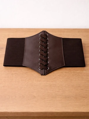 Brunt korsettbälte med snörning - Snyggt brunt korsettbälte med bred resår och dekorativ snörning framtill. Bältet har en unik formad front i skinnimitation och stängs med kardborre bak. Perfekt för att ge outfiten en edgy touch.