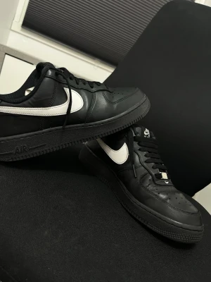 Nike Air Force 1 svart/vit sneaker (går att skanna helt äkta) - Den kommer med box Klassiska Nike Air Force 1 sneakers i svart läder med vit swoosh på sidan. Lågt skaft, svarta skosnören och svart sula. Perfekt för dig som gillar stilrena och tidlösa sneakers med streetkänsla.
