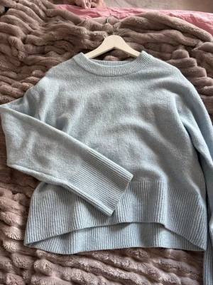 Ljusblå oversized stickad tröja - Mysig ljusblå stickad tröja med oversized passform och breda ribbade muddar vid ärmslut och nederkant. Tröjan har rund halsringning och är tillverkad i ett mjukt material som passar perfekt för kyliga dagar.