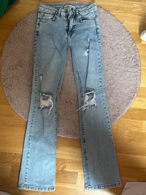 Ljusblå slitna bootcut jeans - Säljer ett par ljusblå bootcut jeans  med slitningar och hål på knäna. Jeansen är mid waitsed, väldigt trendiga och stockholm stil