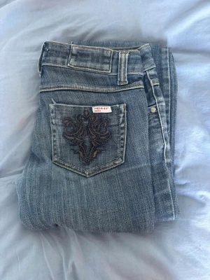 Blå bootcut jeans från ICHI - Säljer ett par blå bootcut jeans från ICHI med snygg broderad bakficka. Jeansen har klassisk femficksdesign, låg midja och slitningar vid benslut. Perfekta för dig som gillar en avslappnad och trendig look.