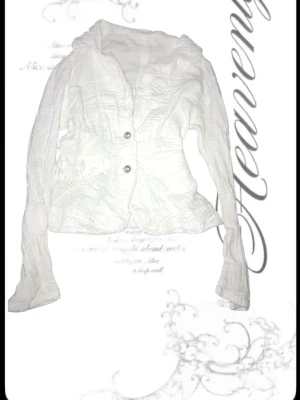 Vit crinkle-blus med broderi - Säljer en vit blus i crinkle-material med långa ärmar och två knappar framtill. Blusen har fina broderade detaljer på ena sidan och ryggen, samt en lätt figursydd passform. Perfekt för dig som gillar en avslappnad men ändå stilren look.