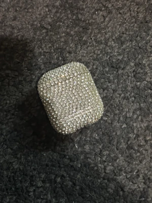 Glittrigt AirPods-fodral med stenar - Säljer ett riktigt blingigt AirPods-fodral täckt av små glittrande stenar. Fodralet är silverfärgat och ger dina hörlurar en lyxig och unik look. Passar perfekt för dig som vill sticka ut och skydda dina AirPods med stil.