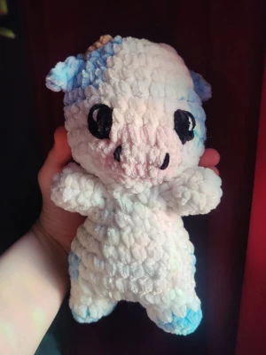 Virkad kossa mjukisdjur blåvit - Supergullig handvirkad kossa i mjuk plysch med stora svarta ögon och små horn. Färgerna är vitt och ljusblått med detaljer i beige och svart. Perfekt som dekoration eller mysig kompis. Unikt handgjort utseende och fluffig känsla.