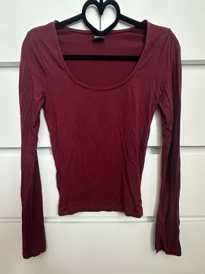 Vinröd långärmad topp - En enkel och stilren vinröd topp med lång ärm och rundad urringning och med slit ärmarna. Toppen har en slim passform.