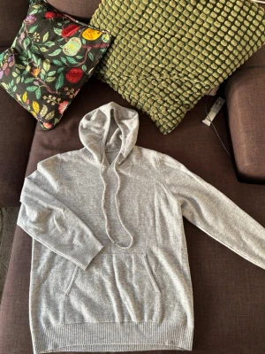 Ljusgrå hoodie med ficka - Mysig ljusgrå bomull och cashmir tröja med huva och dragsnören. Klassisk känguruficka framtill och ribbade muddar vid ärmslut och nederkant. Perfekt för en avslappnad stil och enkel att matcha med andra plagg.