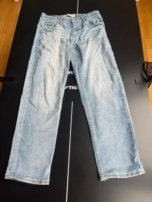 Ljusblå raka jeans från Levi's - 37cm midjemått, 71cm innerbenslängd. Säljer ett par klassiska ljusblå jeans från Levi's med rak passform och fem fickor. Jeansen har en snygg vintage tvätt och är tillverkade i slitstark denim. Perfekta för en avslappnad och trendig look.