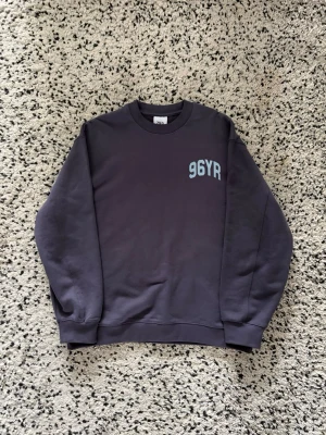 Mörkblå sweatshirt från Zara - Snygg mörkblå sweatshirt från Zara med trycket '96YR' i ljusblått på bröstet. Klassisk rund halsringning och ribbade muddar vid ärmslut och nederkant. Perfekt för en avslappnad och trendig look.