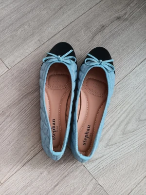 Blå ballerinaskor  - 💫Snygga ballerinaskor från Stephan i ljusblått quiltat tyg med svarta fram och matchande blå rosetter framtill. 🩵🥿Skorna har en mjuk innersula för extra komfort och en klassisk rundad form. Perfekta för dig som gillar en söt och stilig look!🥰 Storlek 38!!!!