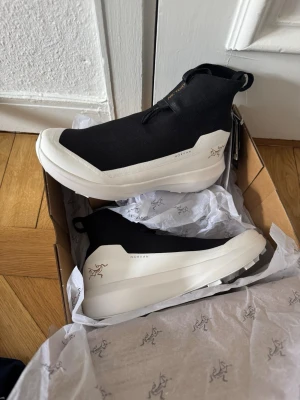 Arc'teryx Norvan 4 Nivalis svarta sneakers - Helt nya och oanvända löparskor från Arc'teryx Norvan 4 med vit chunky sula och minimalistisk design. Till för Bergs- och traillöpning eller snygg att använda som helt vanlig sneaker. Ovandelen är i stretchigt tyg med sockliknande passform och dragflik bak. Sidan har Arc'teryx-logga och Norvan-tryck. 