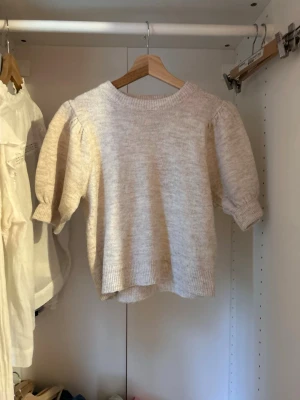 Beige puffärm stickad tröja Gina Tricot - Supersöt beige stickad tröja från Gina Tricot med puffärmar och ribbade muddar. Tröjan har en rund halsringning och är gjord i mjukt material som passar perfekt till höst och vinter. Enkel att matcha med jeans eller kjol för en trendig look.