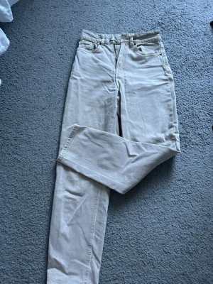 Beige raka jeans med hög/mid midja  - Säljer ett par beige jeans med rak passform och hög/mid midja. Klassisk femficksmodell med knapp och dragkedja framtill. Jeansen är i ett mjukt denimtyg och har en stilren look som passar till det mesta. De är i storlek 34 och kommer från h&m. Pris kan diskuteras 💖