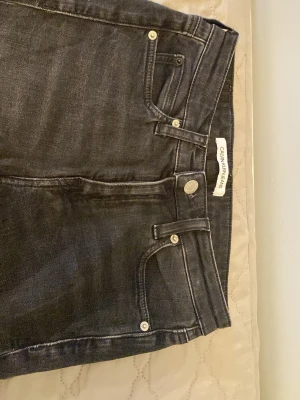 Svarta jeans från Calvin Klein - Snygga svarta jeans från Calvin Klein Jeans med klassisk femficksmodell och raka ben. Jeansen har silverfärgade nitar och knapp, samt diskret logga på linningen. Perfekta till en avslappnad och trendig look.