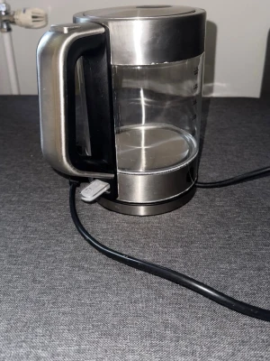Glasvattenkokare i rostfritt stål - Snygg vattenkokare i glas och rostfritt stål med svart handtag. Genomskinlig design med nivåmarkeringar på sidan och sladd för elanslutning. Perfekt för att snabbt koka vatten till te eller kaffe. Tyvärr har den en liten buckla på toppen.