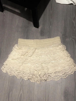 Vit/beige virkade shorts med volang - Snygga shorts med bred resår i midjan och flera lager volang i virkad spets. 