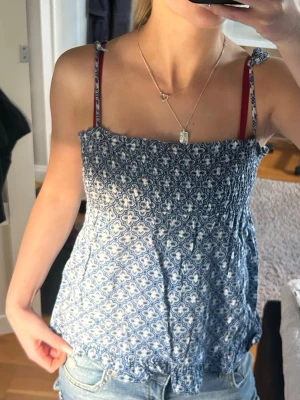 Blå mönstrad linnetopp med knytband - Säljer en blå och vit linnetopp med smock upptill och tunna axelband som knyts på axlarna. Toppen har ett fint mönster i vitt och blått och är perfekt för varma dagar. Passar till jeans eller kjol för en snygg och somrig look💕 Passar perfekt på en xxs eller xs💕
